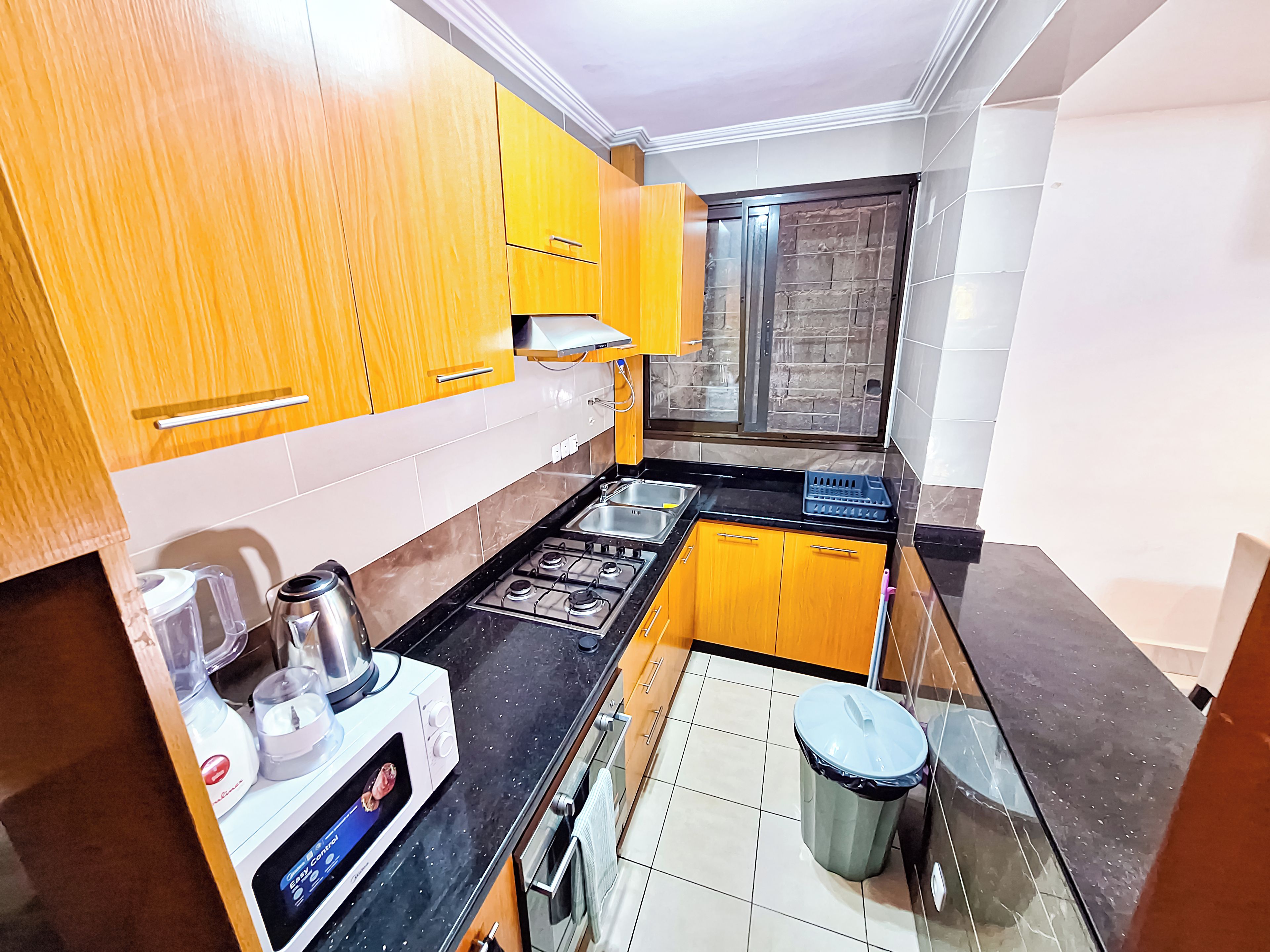 A compact kitchen with wooden cabinets, a gas stove, a sink, and a trash bin.