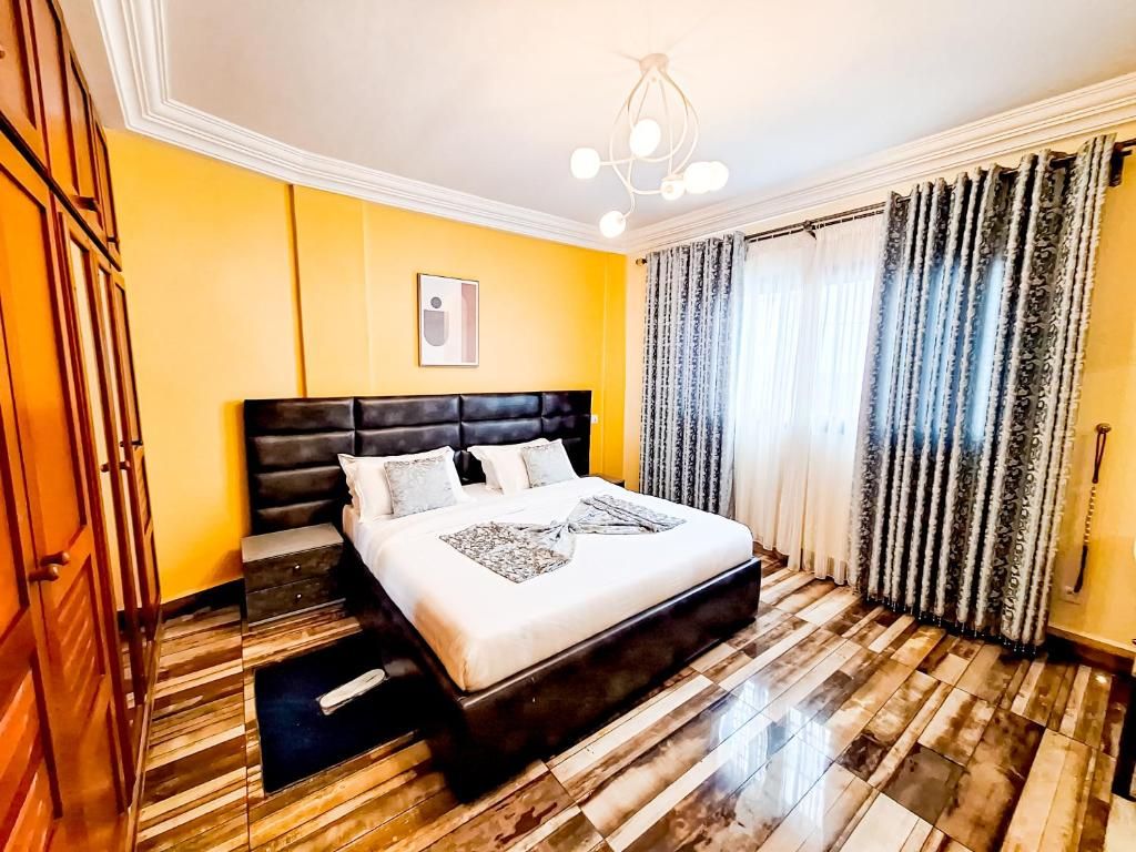 Une chambre d’hôtel avec un grand lit, un plancher en bois, un luminaire au plafond et une fenêtre avec des rideaux.