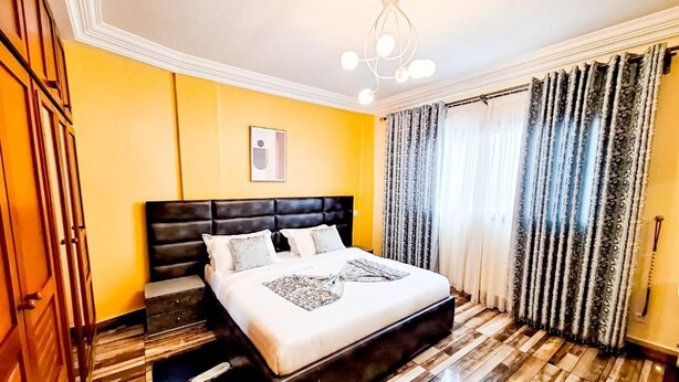 Habitación de hotel con una cama grande, piso de madera, lámpara en el techo y una ventana con cortinas.