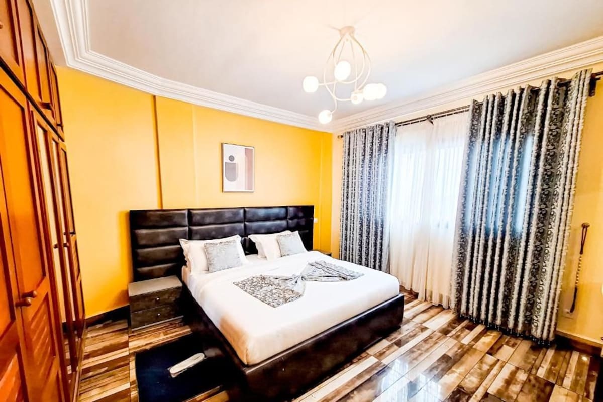 Een hotelkamer met een groot bed, een houten vloer, een plafondlamp en een raam met gordijnen.