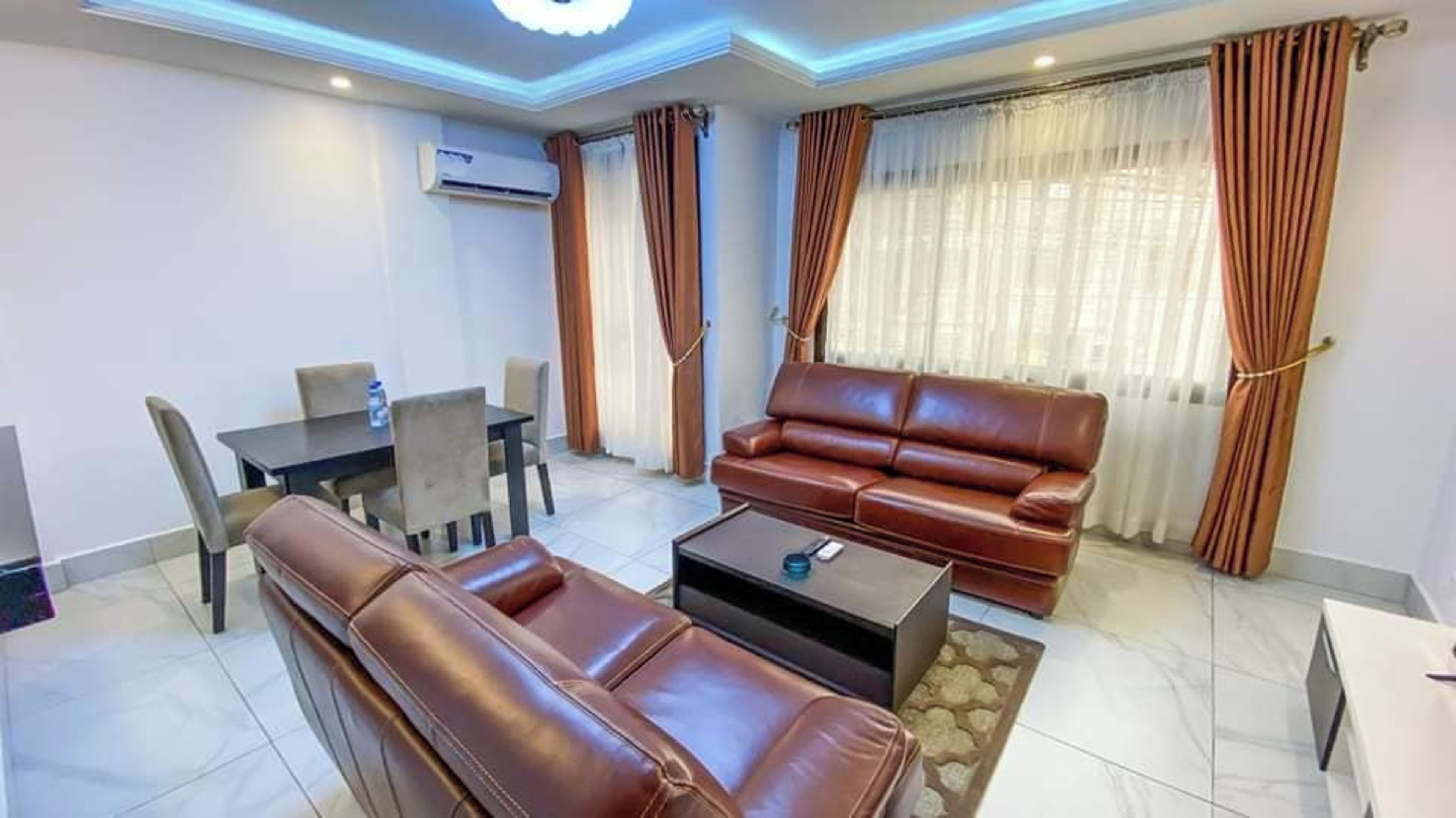 A living room with a brown leather sofa, a coffee table, and a dining area with chairs and a table.