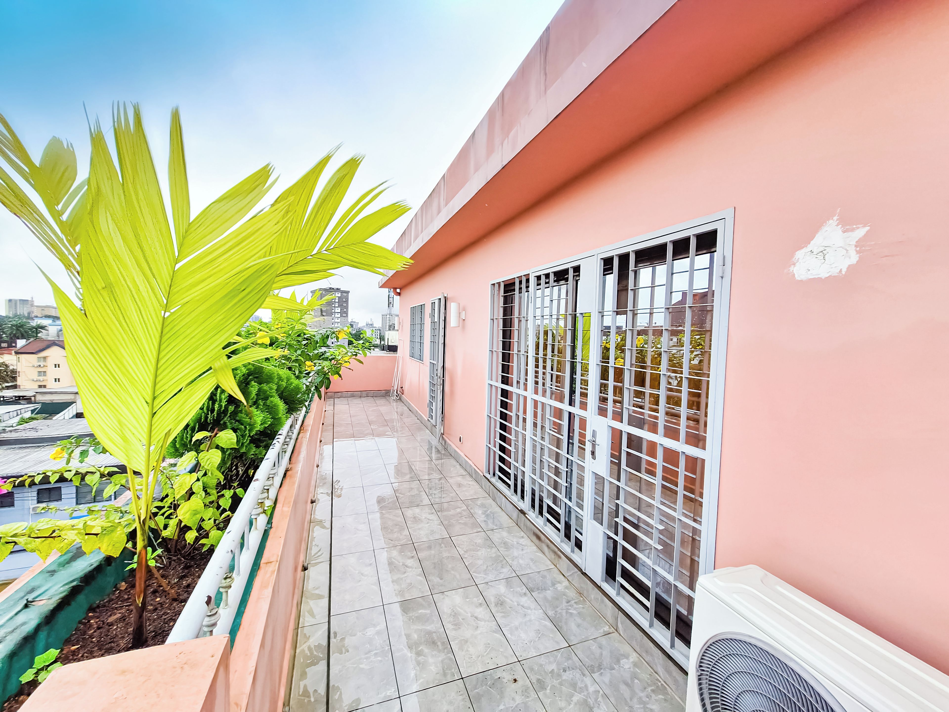 Un balcón con suelo de baldosas, baranda metálica y vista panorámica de la ciudad.