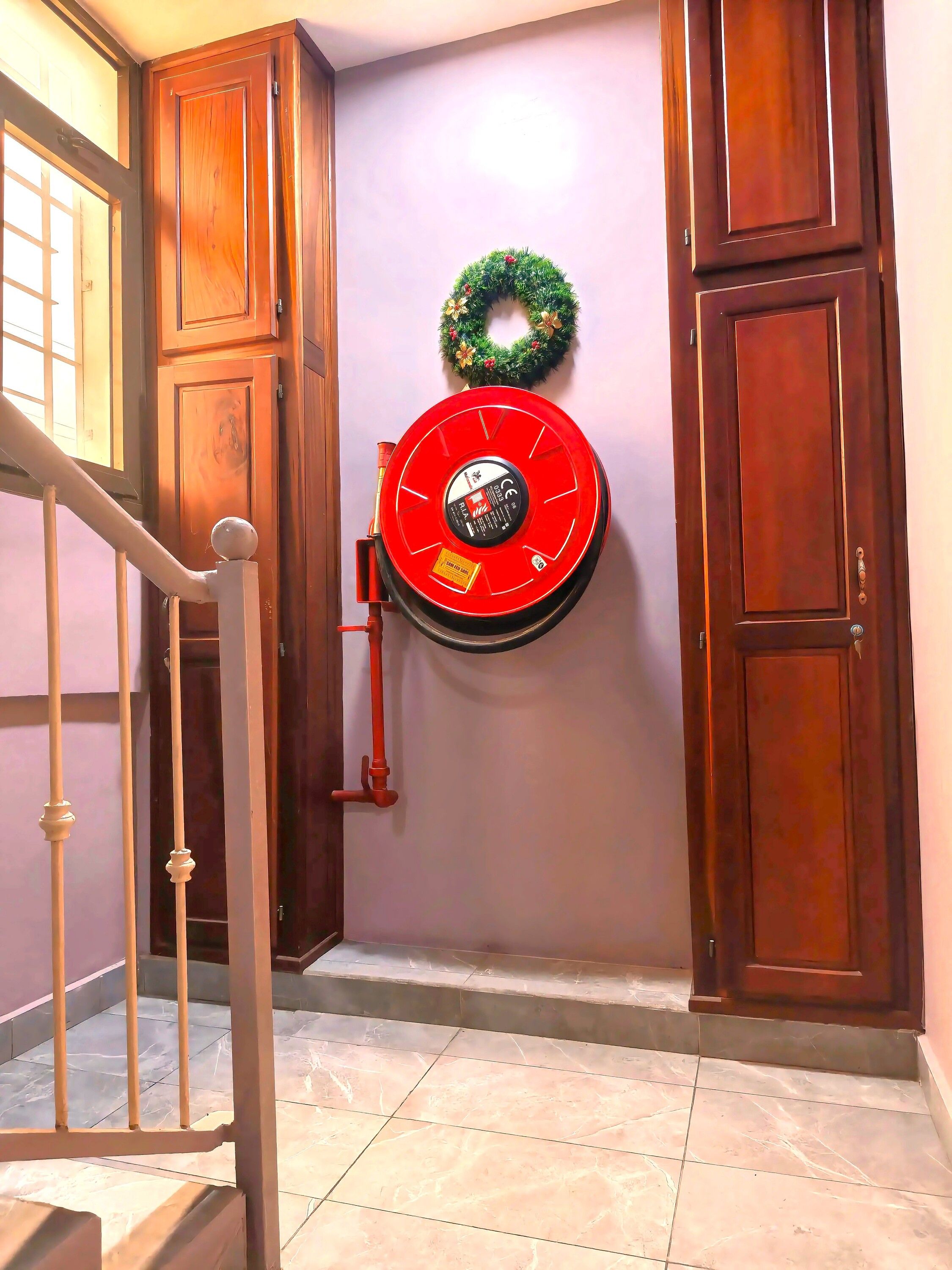 Um corredor com um extintor de incêndio vermelho fixado na parede, portas de madeira e uma escada com corrimão de metal.