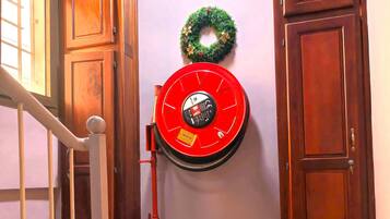 Um corredor com um extintor de incêndio vermelho fixado na parede, portas de madeira e uma escada com corrimão de metal.