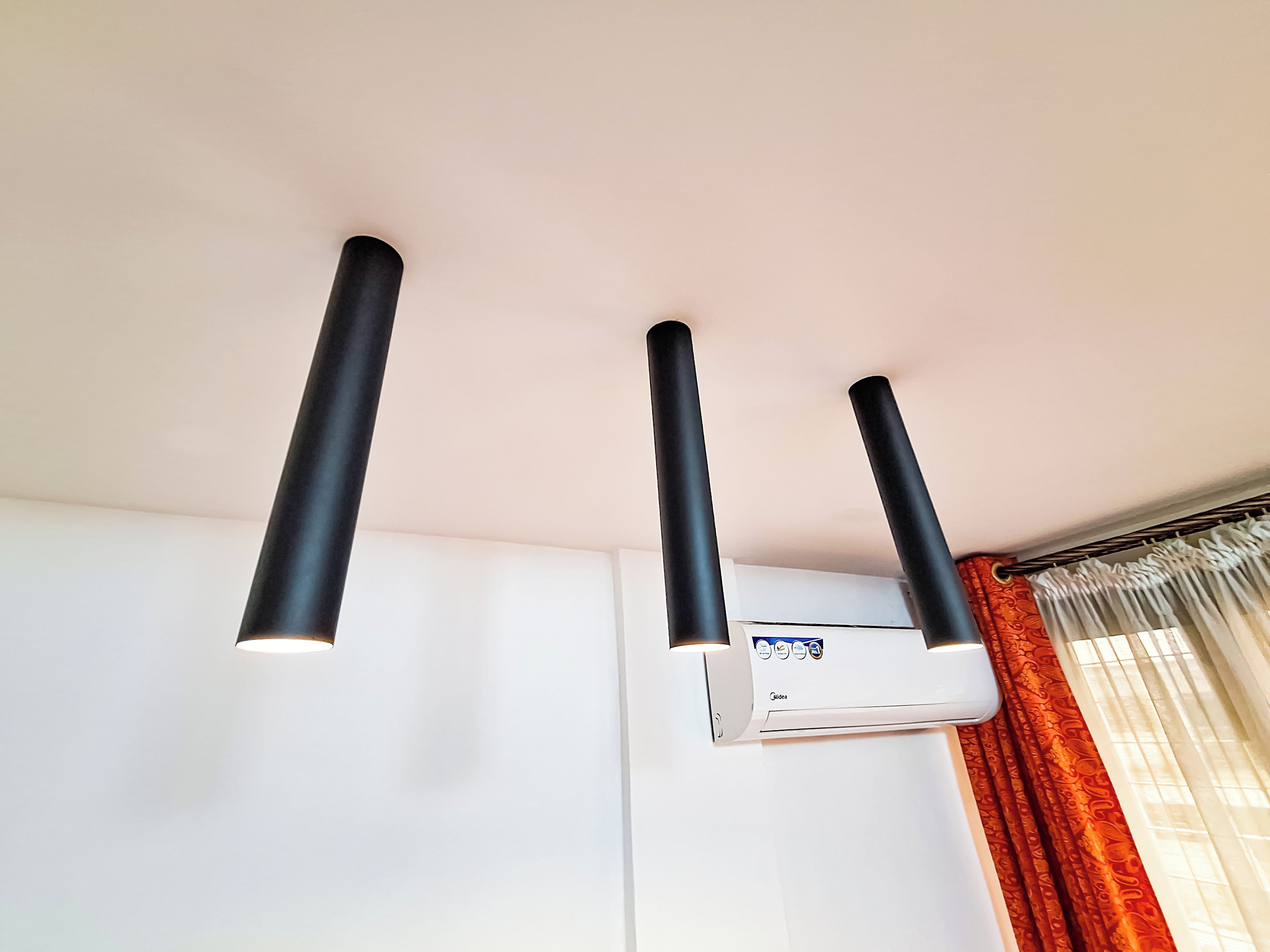 Een aan het plafond gemonteerde airconditioning met drie zwarte, cilindrische ventilatieopeningen.
