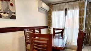 Un comedor con una mesa y sillas de madera, un equipo de aire acondicionado y una ventana con cortinas.
