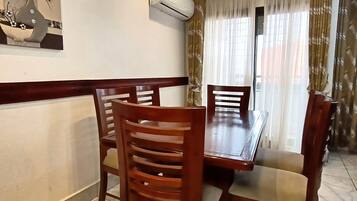 Un coin repas avec une table et des chaises en bois, un appareil de climatisation et une fenêtre avec des rideaux.