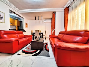 A living room with two red leather sofas, a coffee table, and a dining area with chairs and a table.