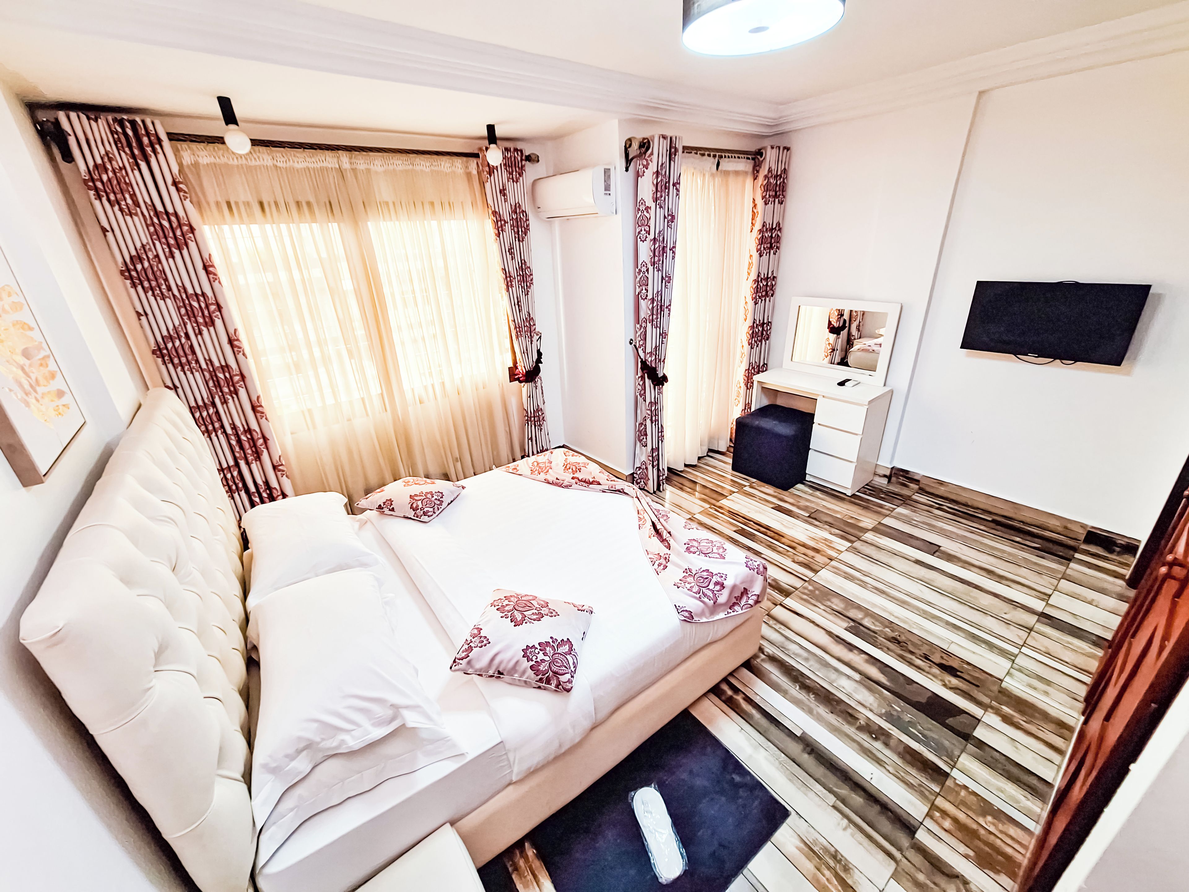 Habitación de hotel con cama, escritorio, silla, televisor y ventana con cortinas.