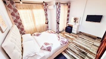 Habitación de hotel con cama, escritorio, silla, televisor y ventana con cortinas.