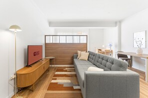 Un saló modern amb un sofà gris, un armari de fusta i una televisió de pantalla plana.