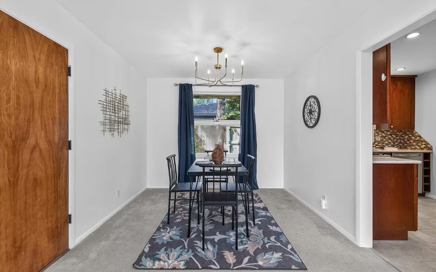 A dining area with a table and chairs, a chandelier, and a view through a window with curtains.