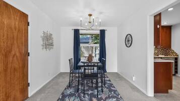 A dining area with a table and chairs, a chandelier, and a view through a window with curtains.