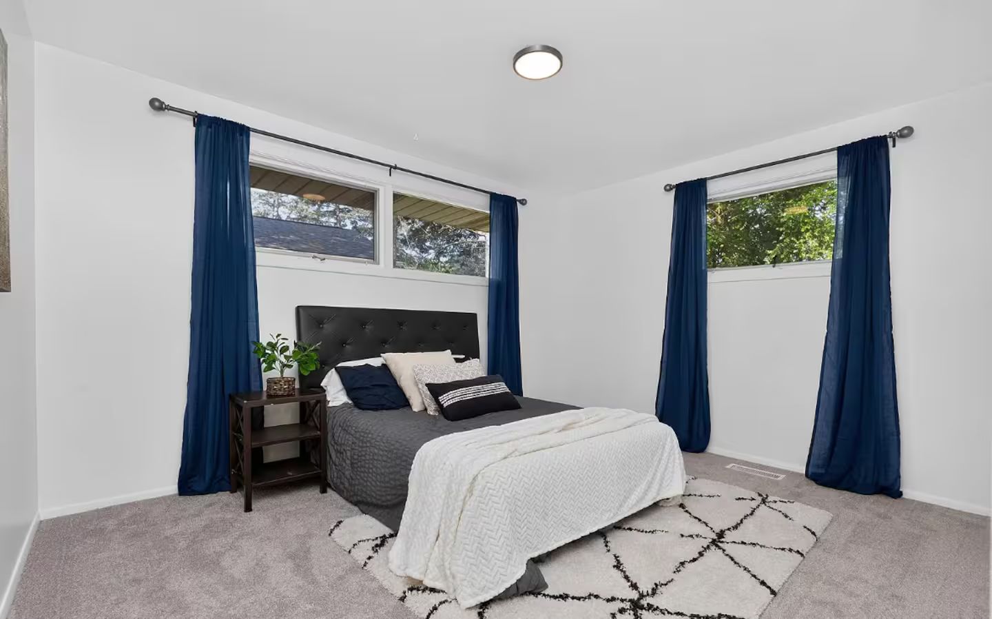 A bedroom with a bed, a nightstand, a window, and curtains.