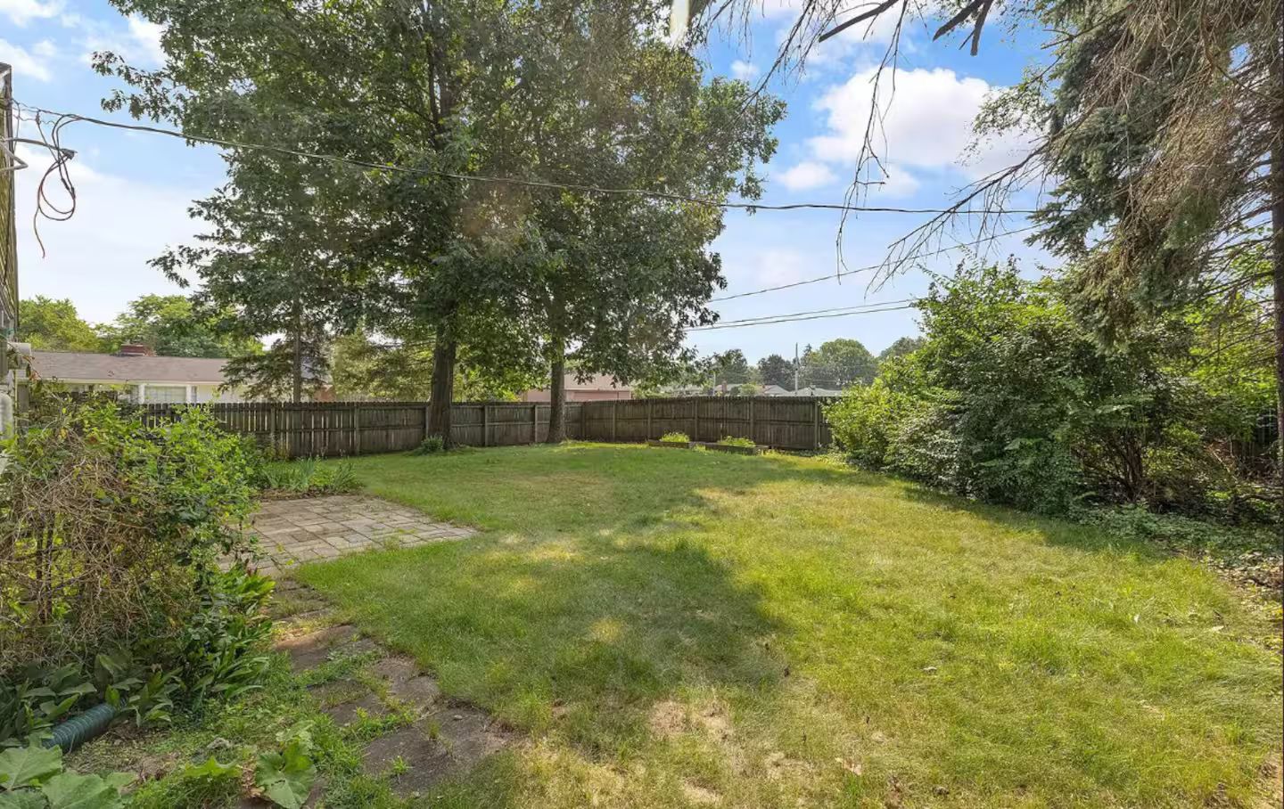 A backyard with a paved area, trees, and a wooden fence.