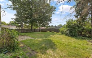 A backyard with a paved area, trees, and a wooden fence. - Sleeps 8 + Walk to ND Campus + Full Amenities (South Bend)