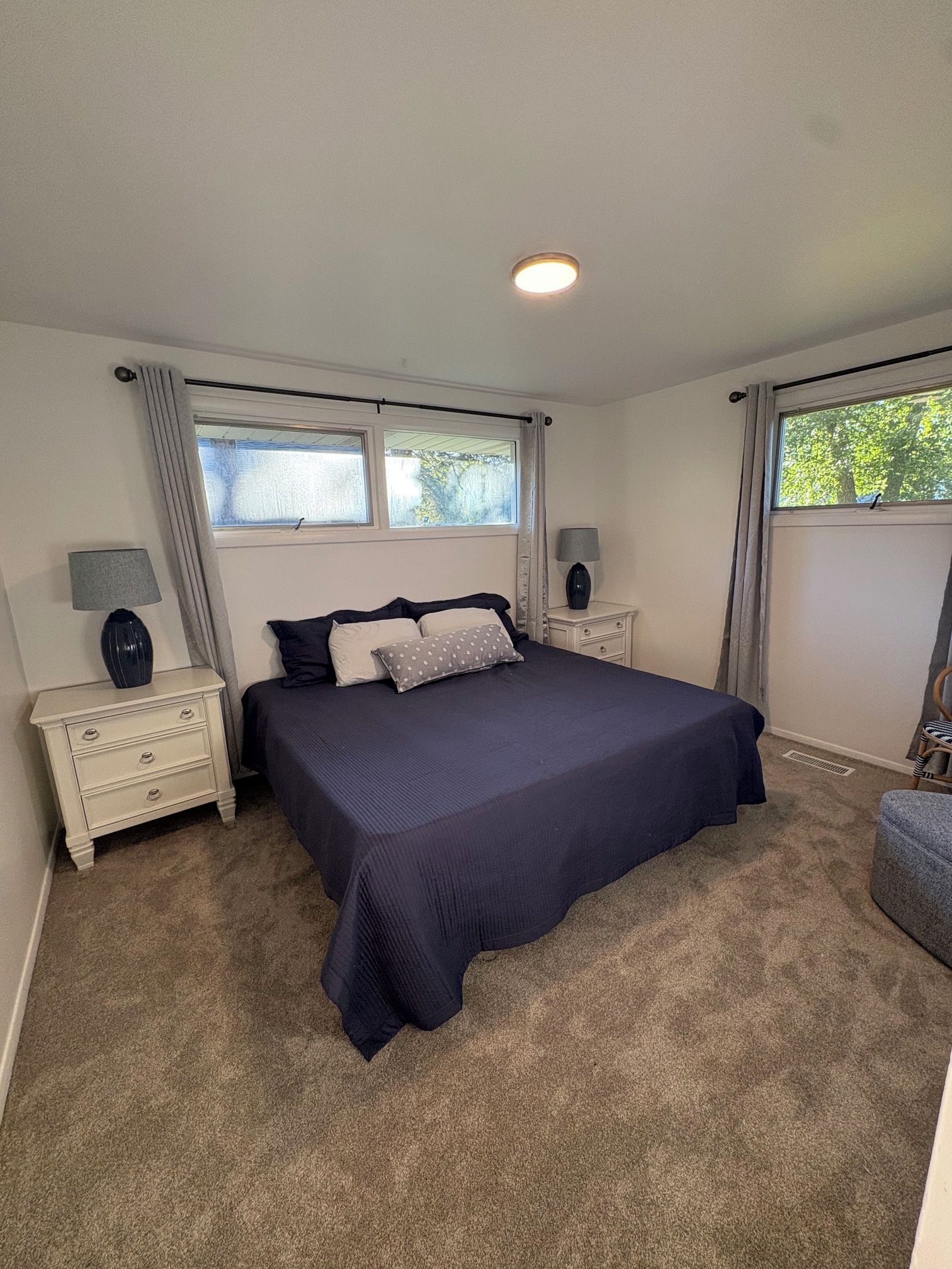 A bedroom with a large bed, two bedside tables with lamps, a window with curtains, and a radiator.