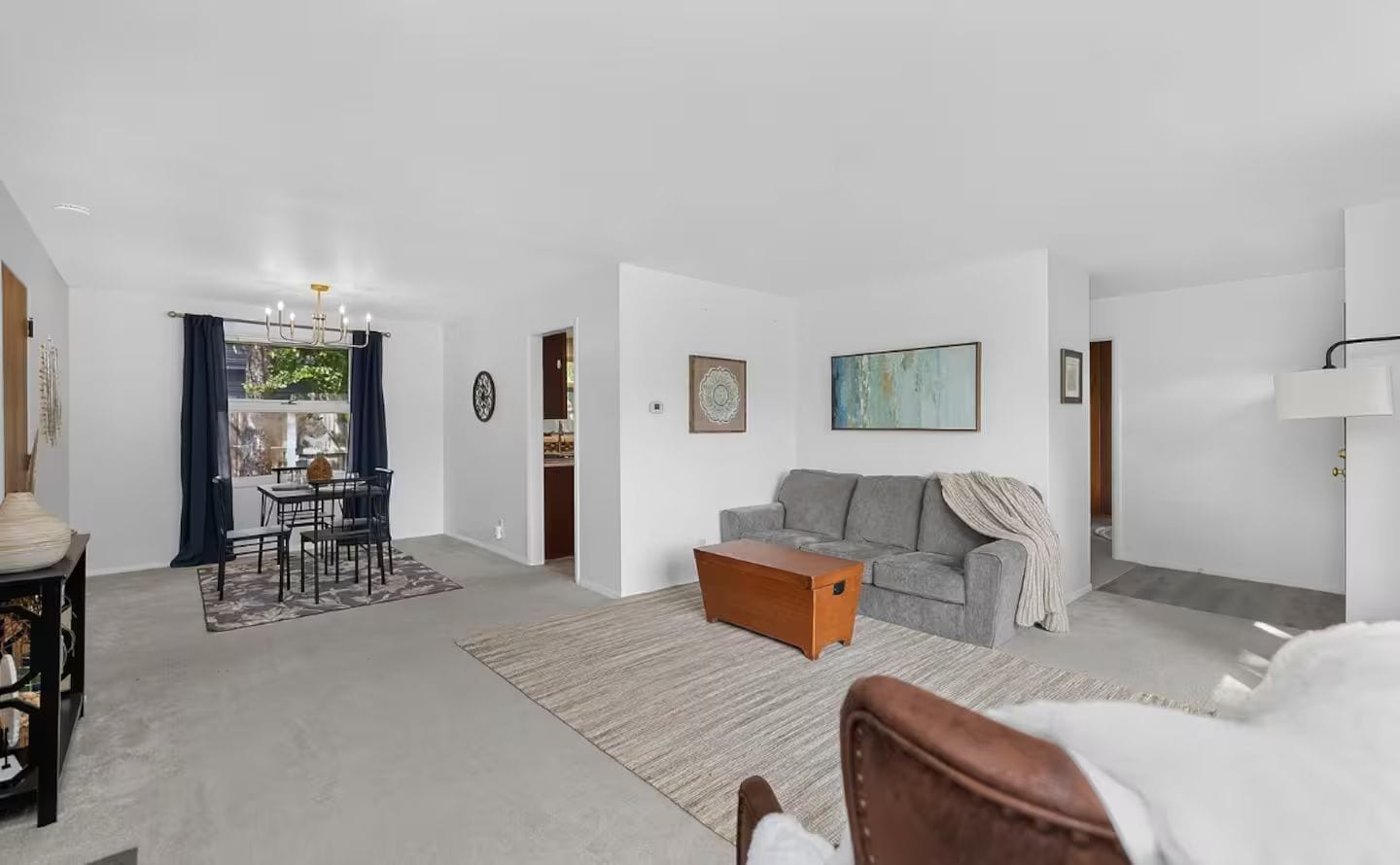 A spacious living area with a grey sofa, a wooden coffee table, and a dining area with a table and chairs.