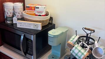 A kitchen with a coffee maker, paper cups, and a microwave.
