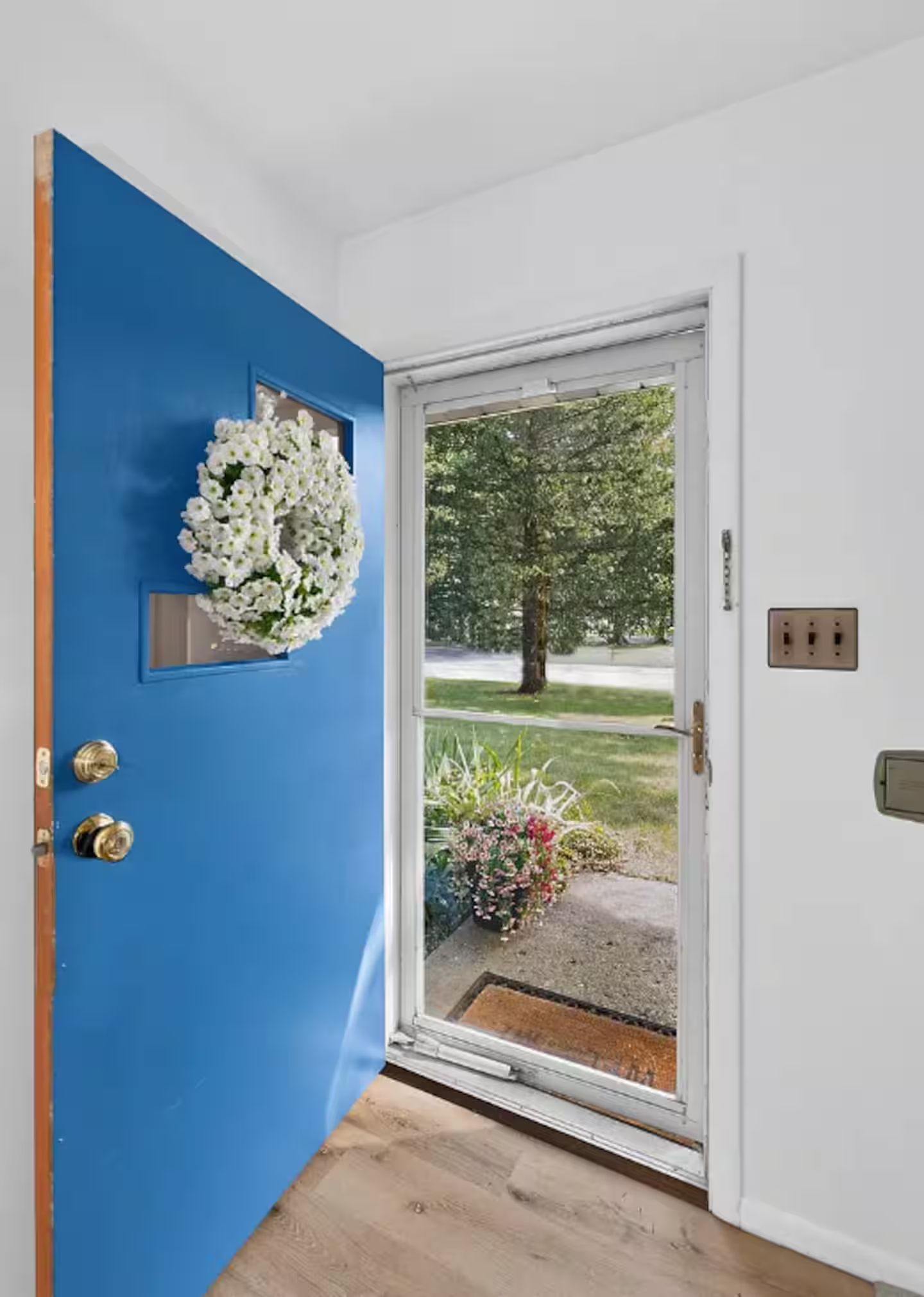 A blue door with a white flower arrangement, a glass door with a view of a garden, and a white wall with a power outlet.