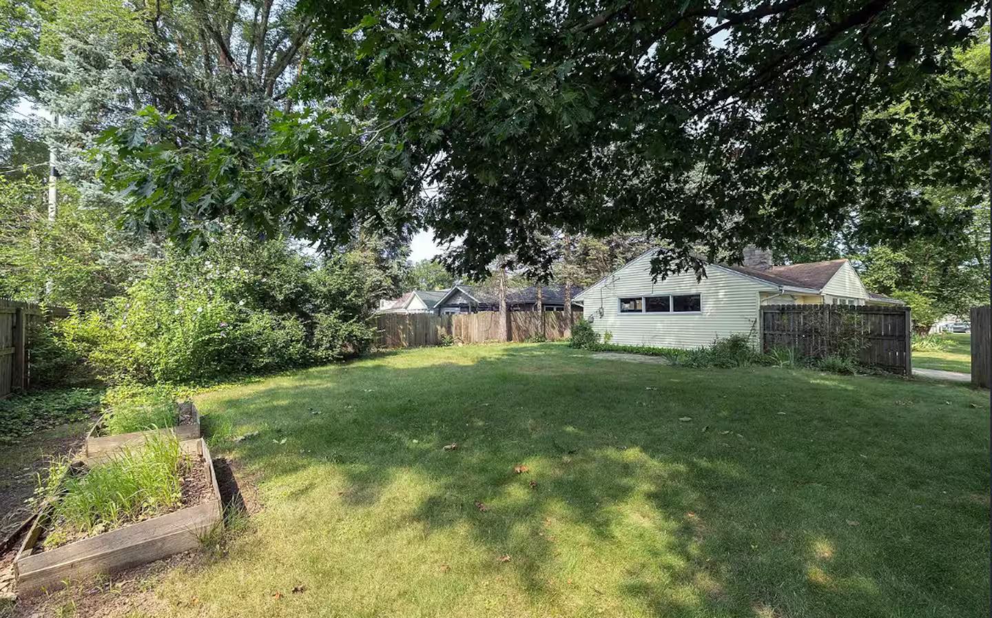 A residential backyard with a house, a wooden fence, and a garden bed.