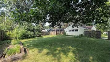 A residential backyard with a house, a wooden fence, and a garden bed.