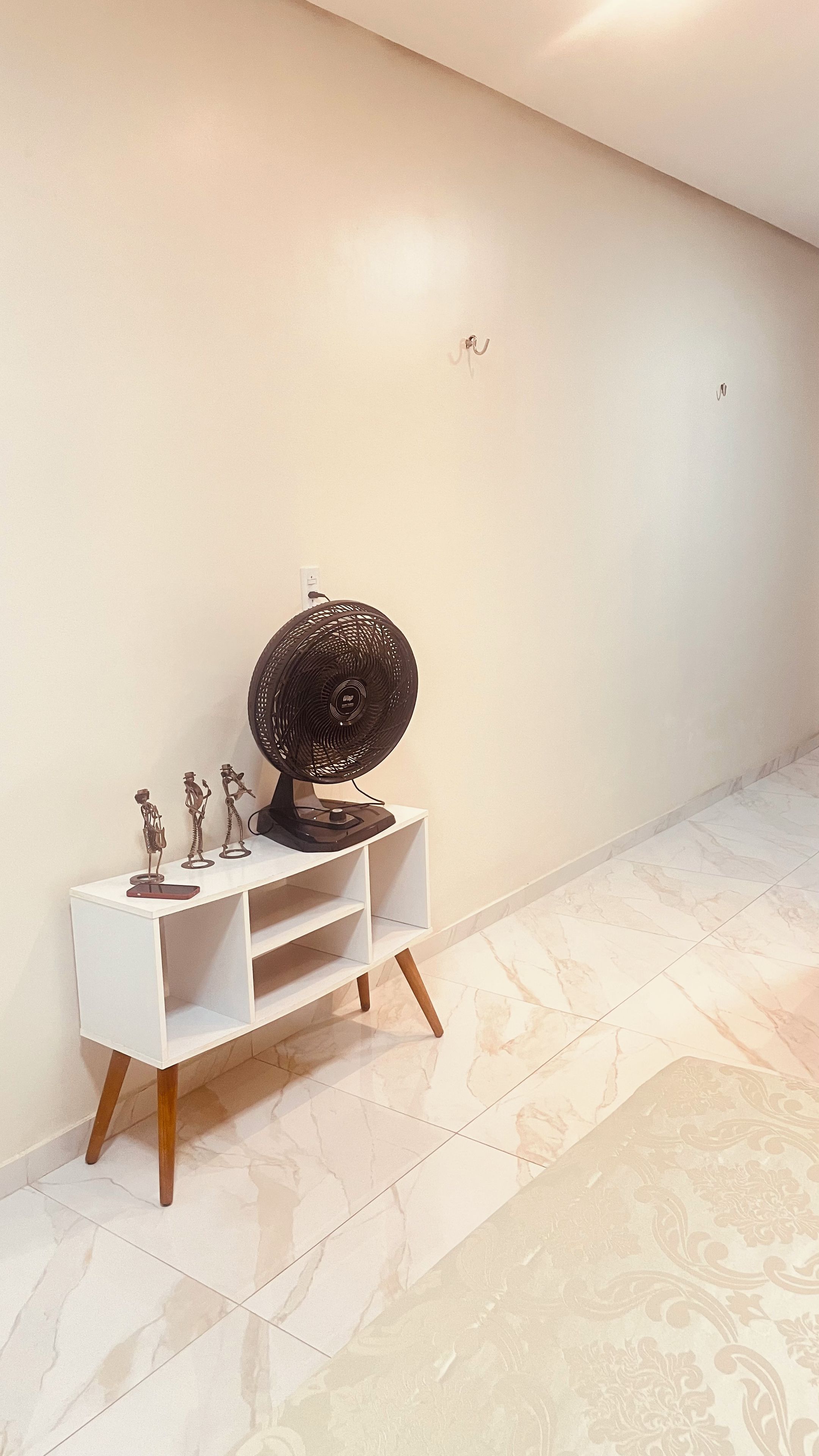 A white TV stand with a black TV and decorative figures, positioned against a plain wall with a tiled floor.