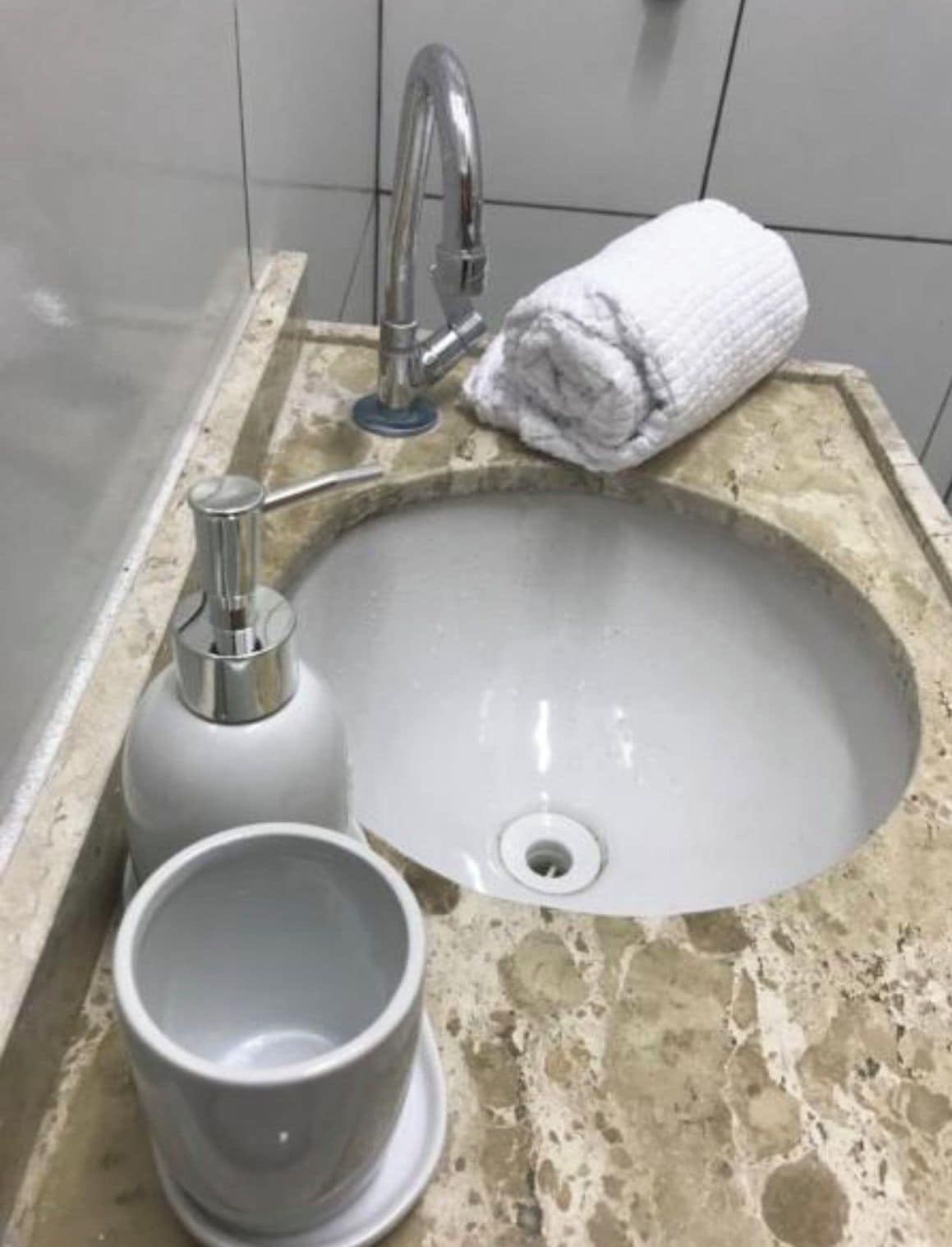 Uma pia de banheiro com torneira, uma toalha e uma xícara.