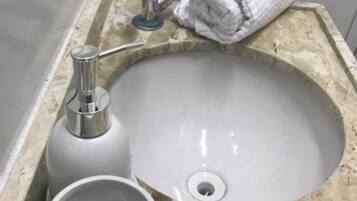 Uma pia de banheiro com torneira, uma toalha e uma xícara.