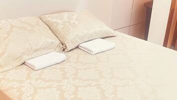 A bed with a patterned bedspread, a folded white towel, and a decorative pillow.