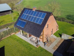 A house with a sloped roof covered in solar panels, a patio with outdoor furniture, and a well-maintained lawn.