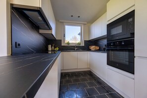 A kitchen with a black marble countertop, white cabinets, a built-in oven, and a window providing natural light.