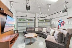 Eine Garage mit einem grauen Ecksofa, einem runden Couchtisch und einem Wandfernseher.