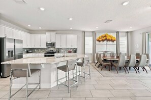A modern kitchen with white cabinets, stainless steel appliances, and a central island with bar stools. - Luxury Home Near Disney w/ Game & Themed Rooms, Waterpark Access - 397SF (Kissimmee)