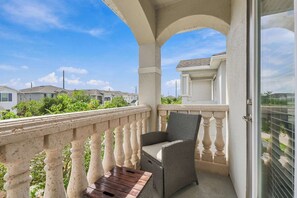 Ein Balkon mit einem Korbstuhl und einem kleinen Tisch, mit Blick auf ein Wohngebiet mit Häusern und Grünflächen.