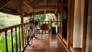 Un balcón de madera con una bicicleta, una silla de mimbre y vistas a zonas verdes.