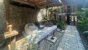 Un área de estar al aire libre con techo de madera y paredes de piedra, un camino empedrado y una pared de piedra con un letrero brasileño.