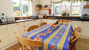 A kitchen with a dining table set for four, a coffee maker, and a window with a view of a garden. - Dunvant (Swanage)