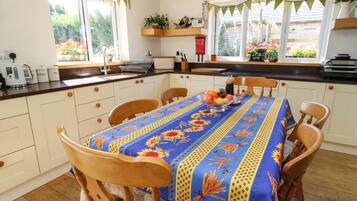 A kitchen with a dining table set for four, a coffee maker, and a window with a view of a garden.