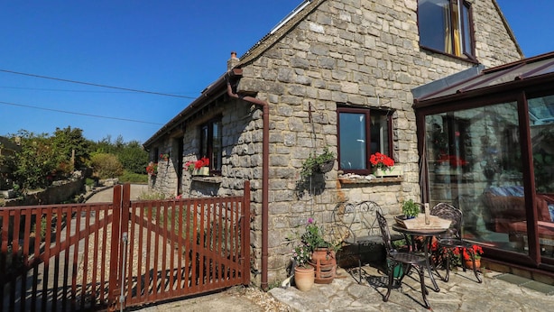 A stone house with a wooden gate, potted plants, and outdoor furniture. - Dunvant (Swanage)