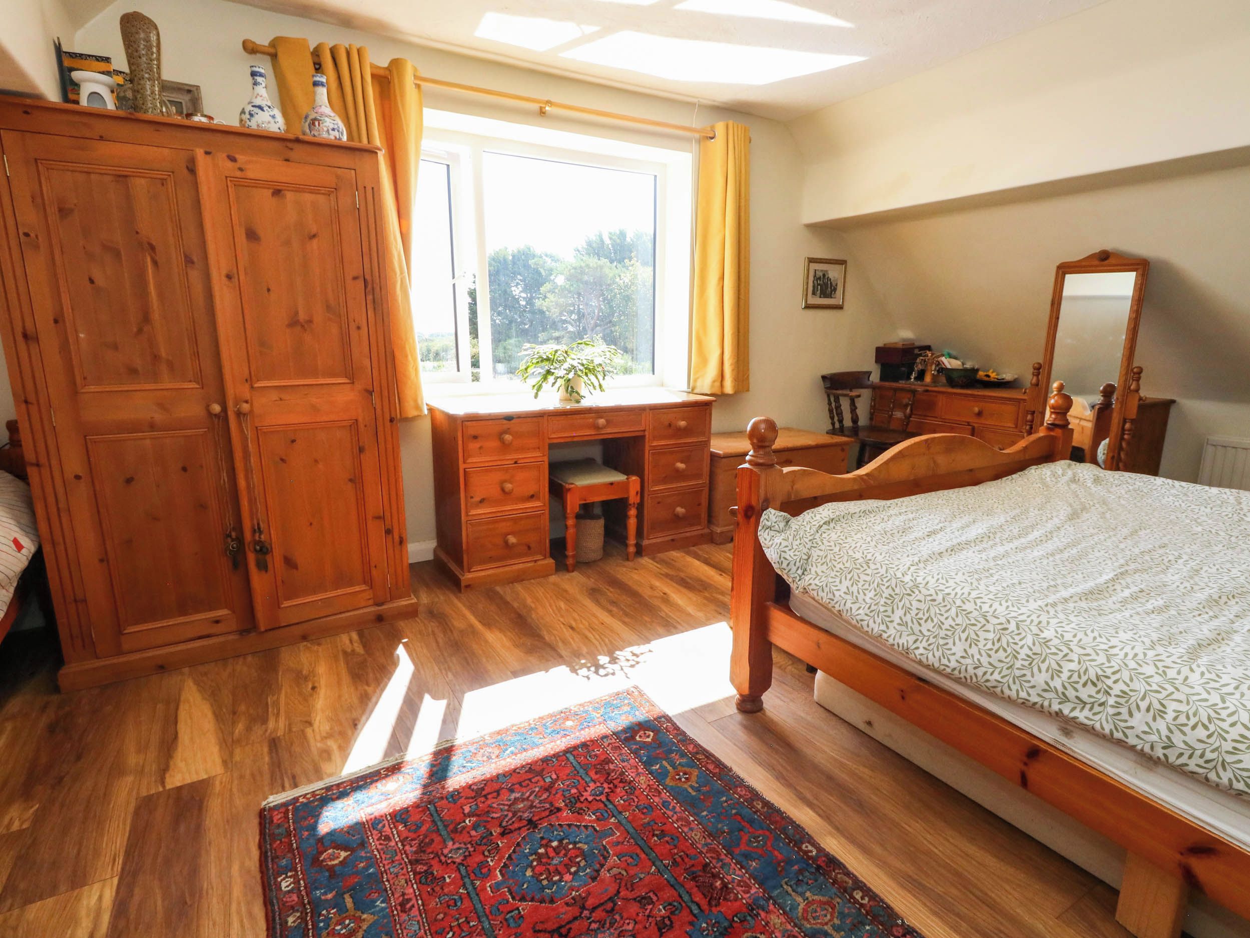 A bedroom with a wooden bed, a desk, a wardrobe, and a window with curtains.