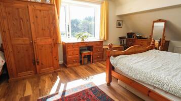 A bedroom with a wooden bed, a desk, a wardrobe, and a window with curtains.