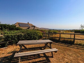 Ein Picknicktisch in einer grünen Wiese mit Blick auf ein Haus mit Solaranlage und blauem Himmel.
