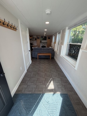 A hallway with a herringbone floor, a bench, a window with a view of trees, and a ceiling with recessed lighting.