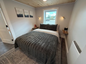 A bedroom with a bed, a window, a nightstand, and wall art.