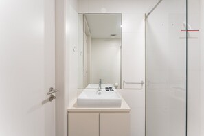 A modern bathroom with a white sink, mirror, and glass shower enclosure. - GuestReady - Nárnia (Porto)