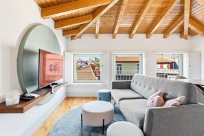 A modern living room with a wooden ceiling, a grey sofa, a round ottoman, and a television on a wooden shelf. - GuestReady - Nárnia (Porto)