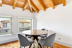 A room with a wooden ceiling, a round table with chairs, and large windows with a view of buildings. - GuestReady - Nárnia (Porto)