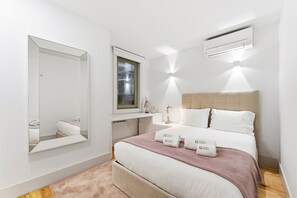 A modern bedroom with a bed, bedside tables, a mirror, a window, and an air conditioning unit. - GuestReady - Nárnia (Porto)