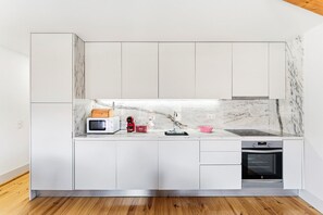 Cozinha moderna com armários brancos, micro-ondas, uma figura de robô vermelha, uma tigela rosa e forno embutido.